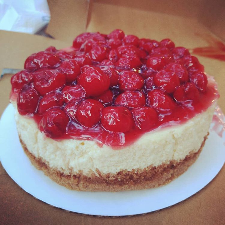 A bakery cheesecake with cherry topping on a dessert table. 